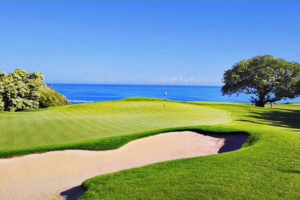 A golf course with a bunker, a flagstick, and a view of the ocean.