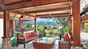 An outdoor seating area with a stone floor, wooden furniture, and a view of a mountainous landscape.