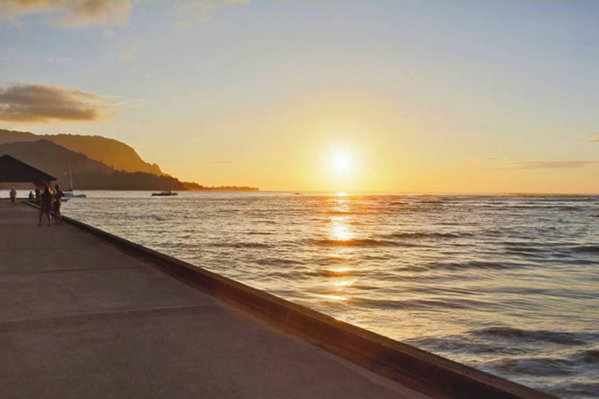 Un atardecer sobre un mar tranquilo con un muelle y una montaña al fondo.