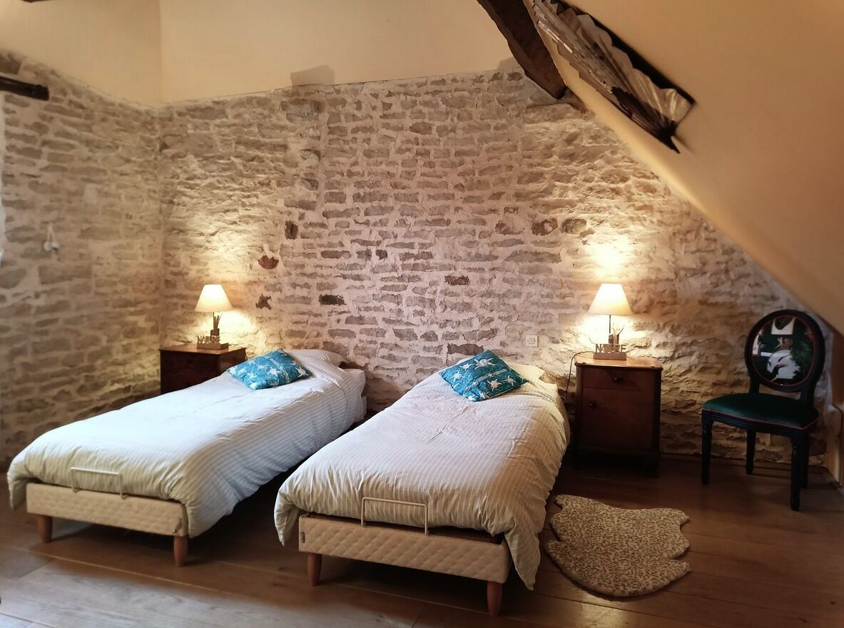 A bedroom with two beds, stone walls, wooden floors, and a chair.