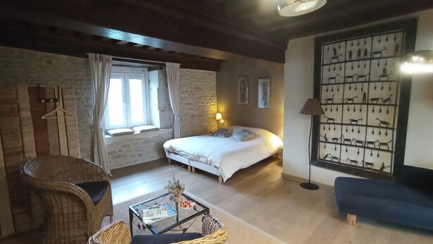 A cozy room with a bed, a wicker chair, a small table, and a wall with animal prints. - La Vallée Verte (Grandchamp)