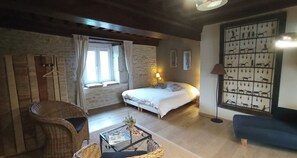 A cozy room with a bed, a wicker chair, a small table, and a wall with animal prints. - La Vallée Verte (Grandchamp)