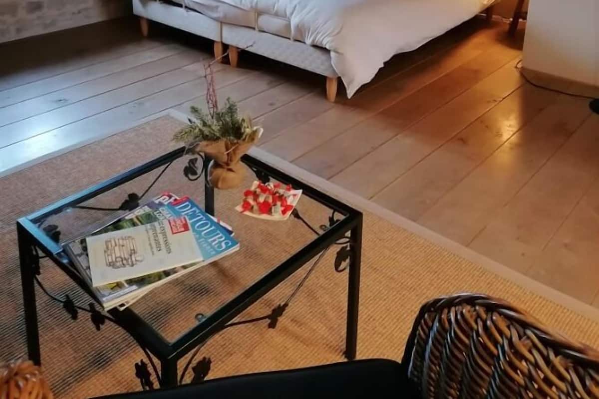 A cozy bedroom with a large bed, a small table with magazines, and a window with curtains.