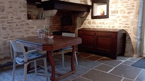 A rustic kitchen with a stone wall, a wooden table, a white chair, and a wooden cabinet. - La Vallée Verte (Grandchamp)