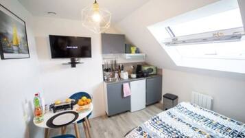 A compact room with a bed, a dining table, a TV, a kitchenette, and a window.