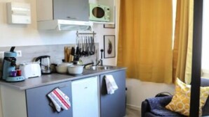 A compact kitchen with modern appliances and a dining area with a small table and sofa. - Residence Kelys (Boulogne-sur-Mer)