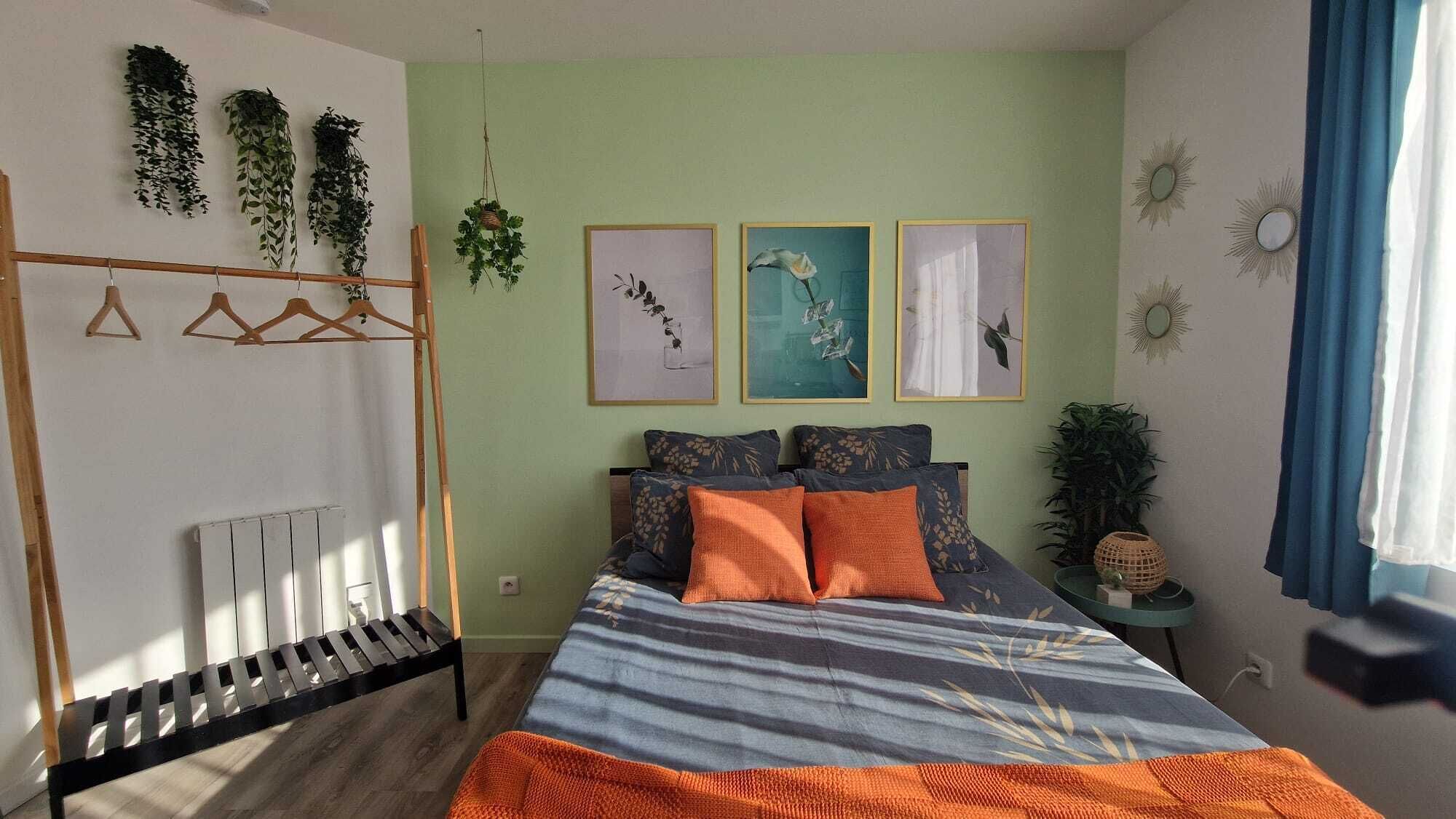 A bedroom with a bed, a radiator, a wooden hanger rack, and wall-mounted plants.
