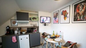 A compact kitchen with a microwave, coffee maker, and a small refrigerator. There is a dining table with chairs and a TV mounted on the wall. - Residence Kelys (Boulogne-sur-Mer)