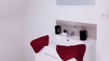 A small, white bathroom with a single sink, a mirror above it, and a trash can to the left.