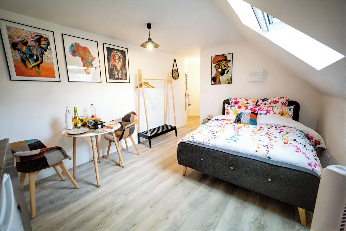 A bedroom with a bed, a desk, a chair, and artwork on the walls.
