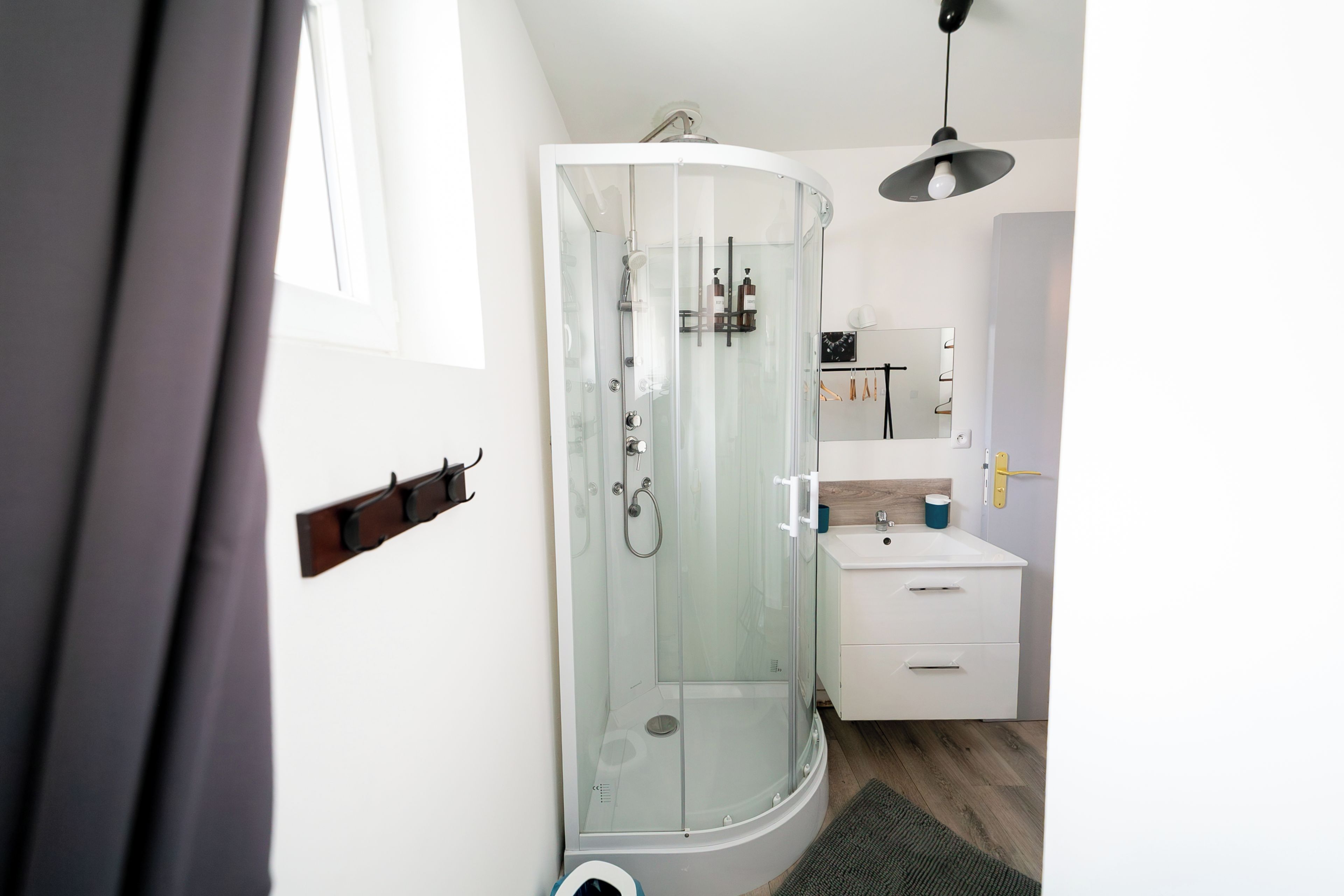 Un bagno moderno con doccia vetro, un mobile lavabo bianco e una lampada a sospensione.