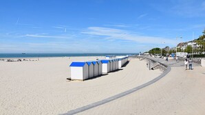 A beach with a row of white beach huts with blue roofs, a clear sky, and a calm sea in the background. - Residence Kelys (Boulogne-sur-Mer)