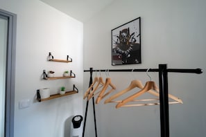 Une pièce comprenant un étendoir à linge en métal noir, des étagères en bois ornées d’objets décoratifs et une œuvre d’art encadrée accrochée au mur.