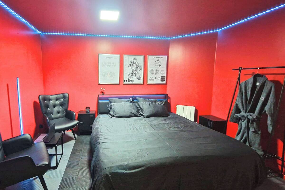 A room with a bed, two chairs, a radiator, and a coat rack.