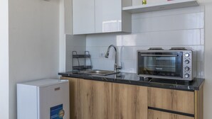 A compact kitchen with white cabinets, a black countertop, a built-in toaster oven, and a small refrigerator. - Yelloscape/ Gemmayze (Beirut)