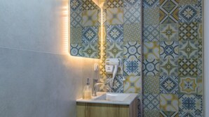 A bathroom with a sink, a mirror, and a hand dryer. The wall has a patterned tile design. - Yelloscape/ Gemmayze (Beirut)