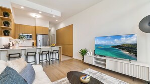 Una sala moderna con un televisor grande, un sofá y una cocina con armarios de madera y un taburete de bar.