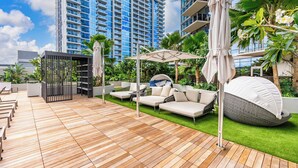 Un patio en la azotea con mobiliario exterior, una zona de estar cubierta y vistas a un edificio alto.