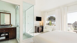 A hotel room with a bed, a bathroom with a glass shower, a TV, and a view of the outside. - Bright Cayucos Bungalow Steps to Beach & Pier | 3BR w/ Shared Firepit Lounge (Cayucos)
