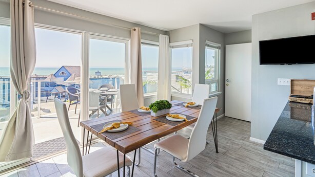 A dining area with a wooden table, white chairs, and a view of the ocean.