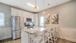 A modern kitchen with white cabinets, stainless steel appliances, and a central island with bar stools. - Sleeps 33! 4 Condos, Walk to the Beach, Resort-Style Pool, Endless Summer Resort (Port Aransas)