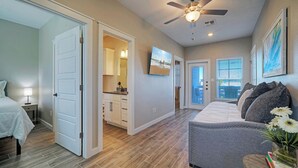 A spacious living area with a gray sofa, a ceiling fan, and a view of the city through large windows. - Sleeps 33! 4 Condos, Walk to the Beach, Resort-Style Pool, Endless Summer Resort (Port Aransas)