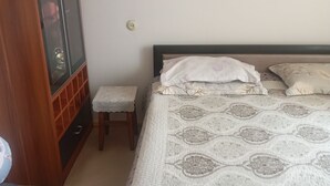 Een slaapkamer met een bed, een houten garderobe, een klein krukje en een stopcontact.
