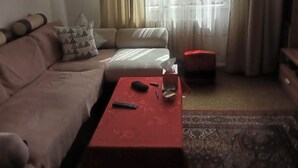 Een woonkamer met een bank, een rode voetenbankje, een afstandsbediening en een zakdoos.