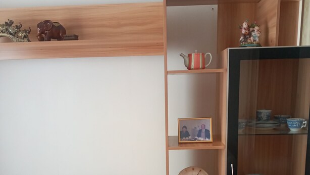 Een houten plank met decoratieve objecten, een televisietoestel en een glazen kast met borden.
