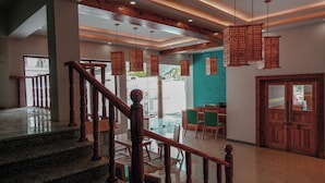 A hotel lobby with a staircase, wooden railings, hanging lanterns, and a seating area with chairs and tables. - The Rangjung Hotel (Leh)