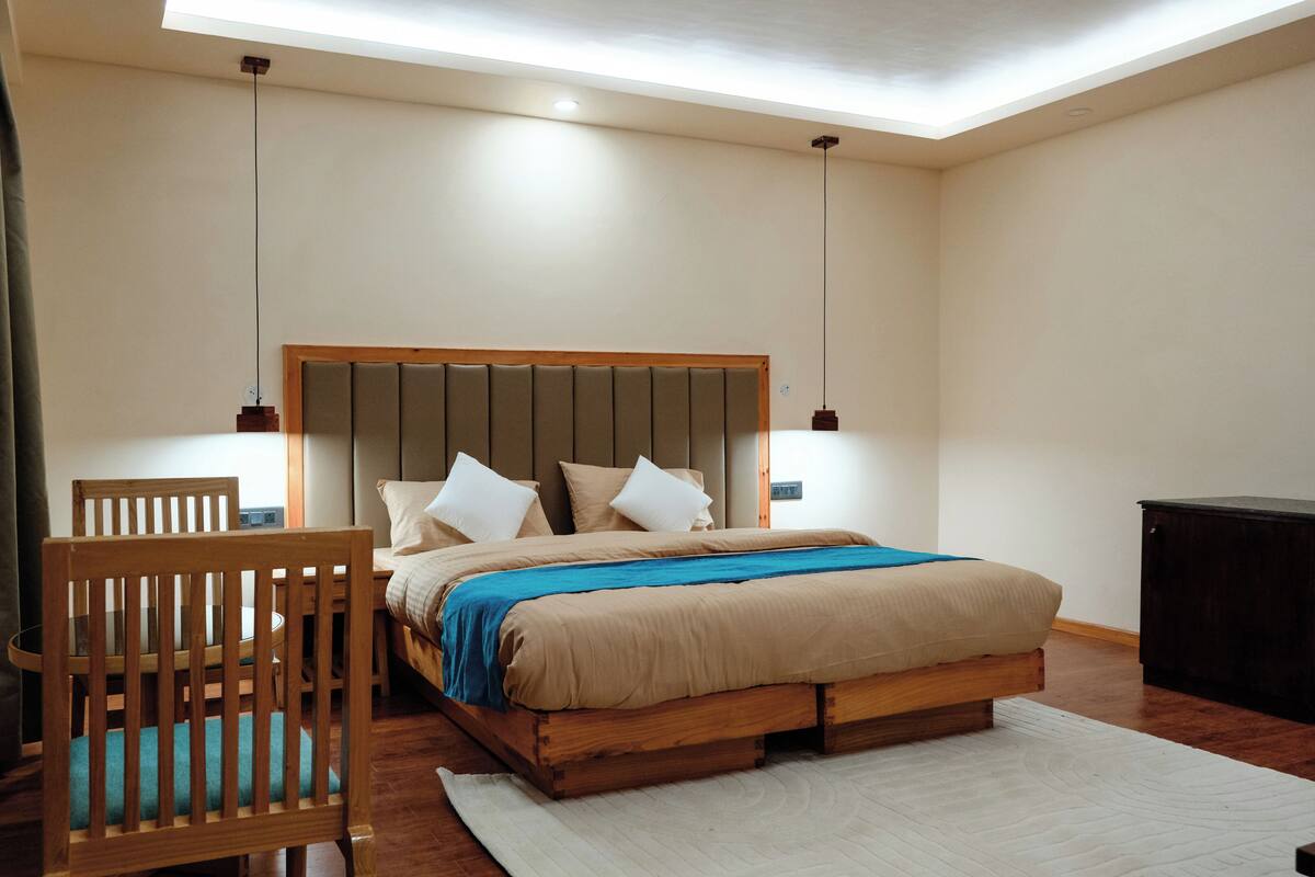 A bedroom with a wooden bed, a wooden chair, a desk, and a desk lamp.
