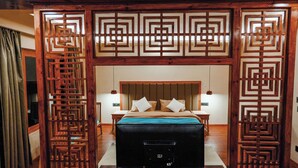 A bedroom with a bed, nightstands, and a wooden partition with geometric patterns. - The Rangjung Hotel (Leh)