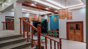 A staircase with wooden balusters, a dining area with chairs and tables, and a reception desk. - The Rangjung Hotel (Leh)