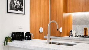 A modern kitchen with a stainless steel sink, wooden cabinets, and a coffee maker. - The Vinyl Abode | Free Parking + 5-Minute CBD Walk (West Melbourne)