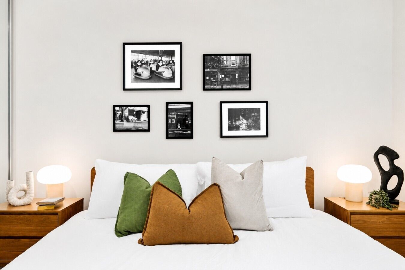A bedroom with a bed, pillows, framed pictures on the wall, and bedside lamps.