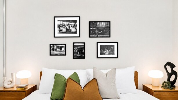 A bedroom with a bed, pillows, framed pictures on the wall, and bedside lamps. - The Vinyl Abode | Free Parking + 5-Minute CBD Walk (West Melbourne)