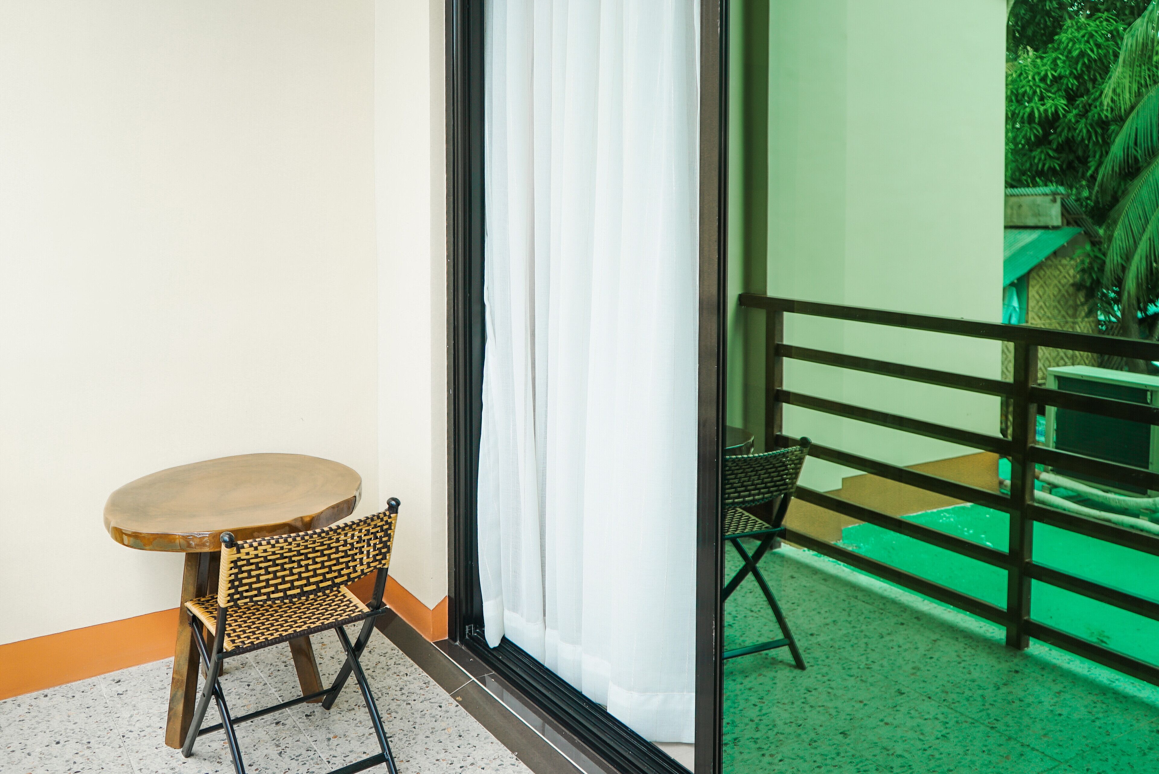 Une petite pièce avec une table en bois et une chaise en osier, une porte-fenêtre coulissante et un balcon doté d’un sol recouvert d’herbe.