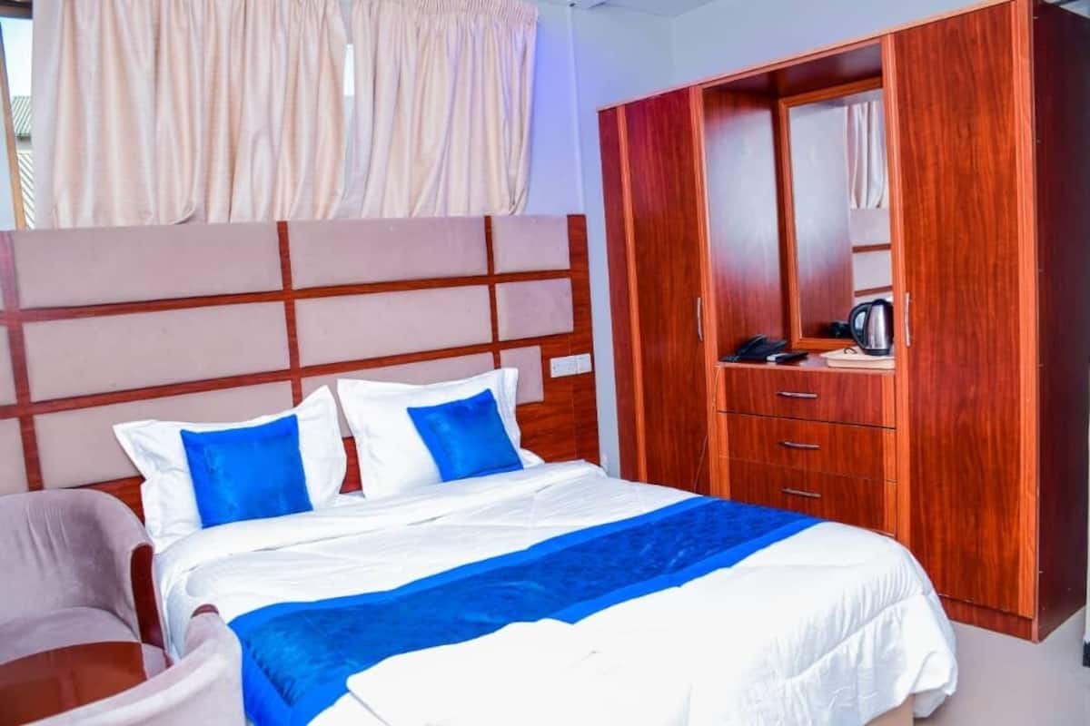 A hotel room with a bed, a wooden wardrobe, a mirror, and a window with curtains.