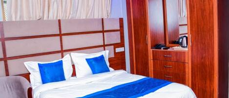 Una habitación de hotel con cama, armario de madera, espejo y ventana con cortinas.