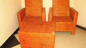 Twee rieten stoelen met een klein tafeltje ertussen, geplaatst tegen een effen muur.