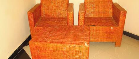Two wicker chairs with a small table in between, placed against a plain wall.