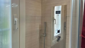 A modern bathroom with a glass shower enclosure, a control panel, and a towel rack.