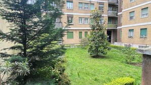 A multi-story residential building with a courtyard featuring a lawn, trees, and shrubs.