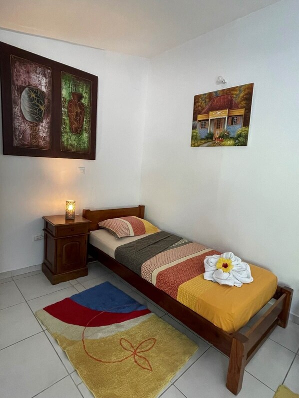 Een slaapkamer met een bed, een nachtkastje, een wandlamp en twee kunstwerken in lijsten.