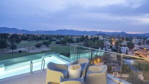 A rooftop terrace with a pool, lounge chairs, and a view of a golf course and cityscape.