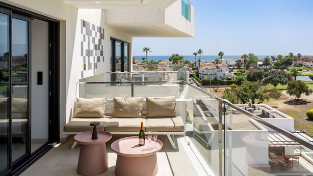A balcony with a sofa, two round tables, and a bottle of champagne.