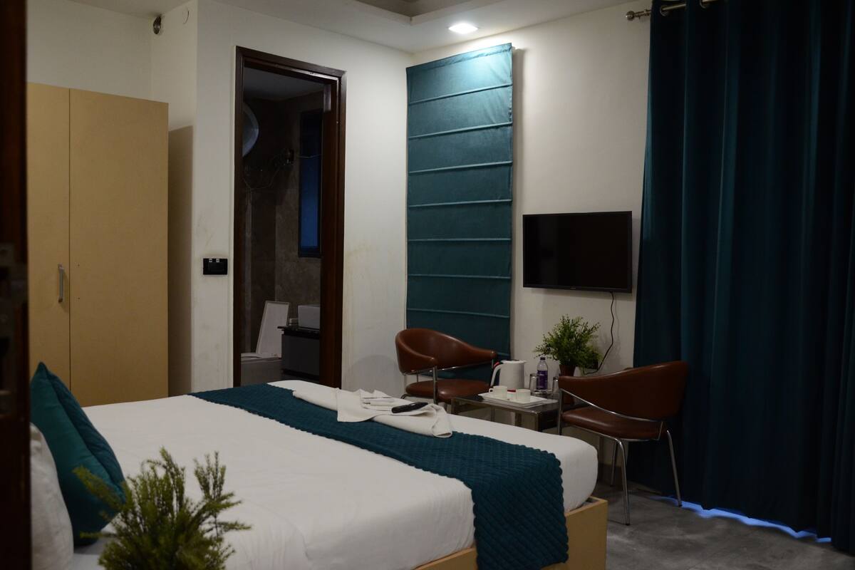 Habitación de hotel con una cama, dos sillas, un escritorio, un televisor y una puerta que da a un baño.