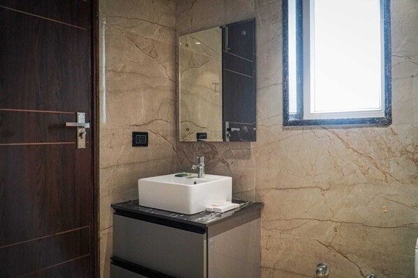 A bathroom with a marble wall, a white sink, a mirror, and a door. - Leaf Studio Hospitalities Near Medanta (Gurugram)