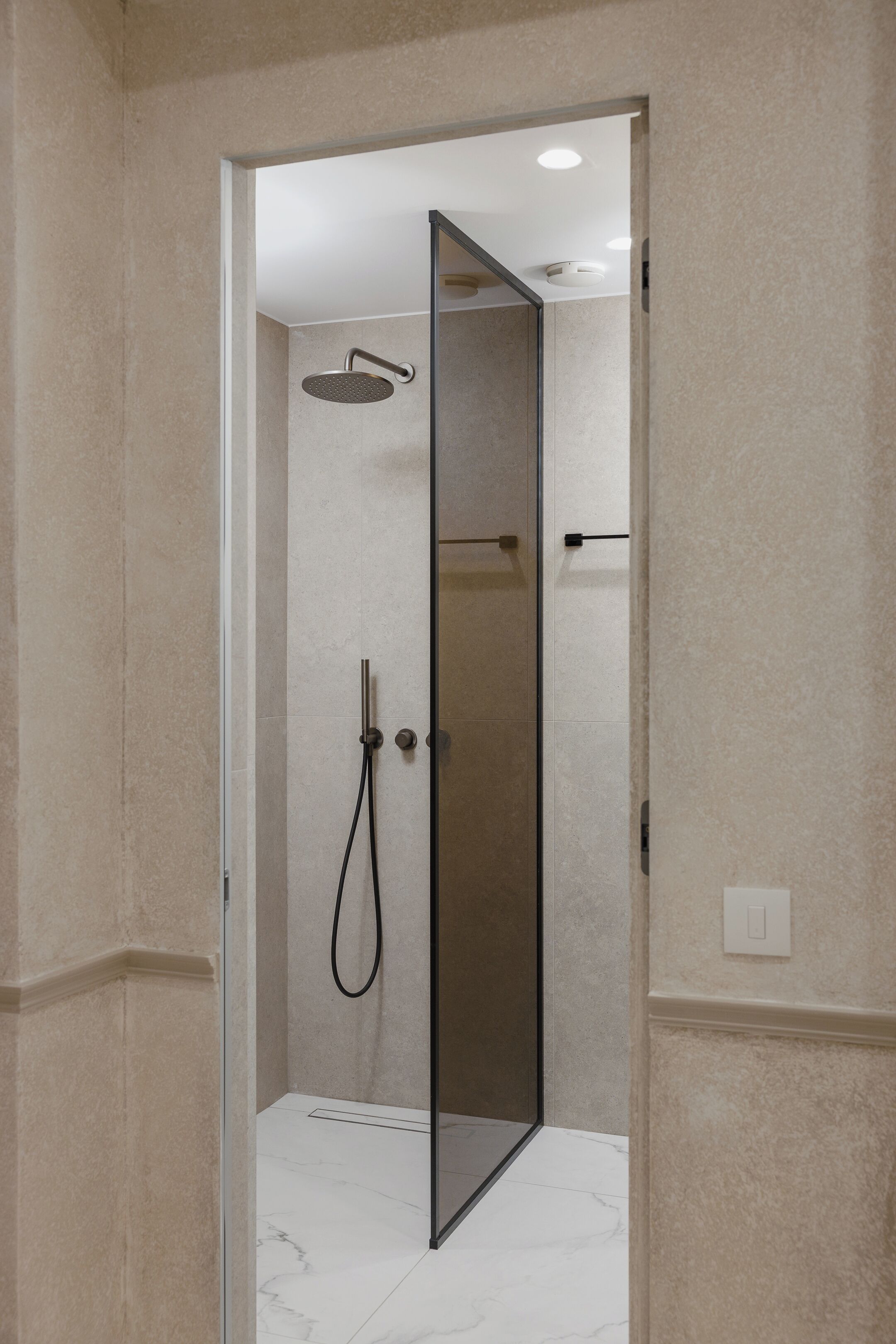 A modern shower with a glass door, a handheld showerhead, and a wall-mounted faucet.