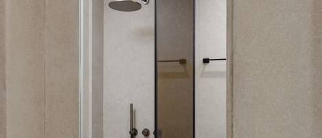 A modern shower with a glass door, a handheld showerhead, and a wall-mounted faucet.